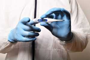 medical worker with surgical gloves holding a thermometer