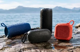 Blue, Black And Red Waterproof Bluetooth Speakers On A Rock Beside A Sunny Lake