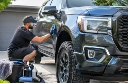 Man Detailing The Side Of A Dark Pickup Truck In A Driveway Next To A Wash Bucket